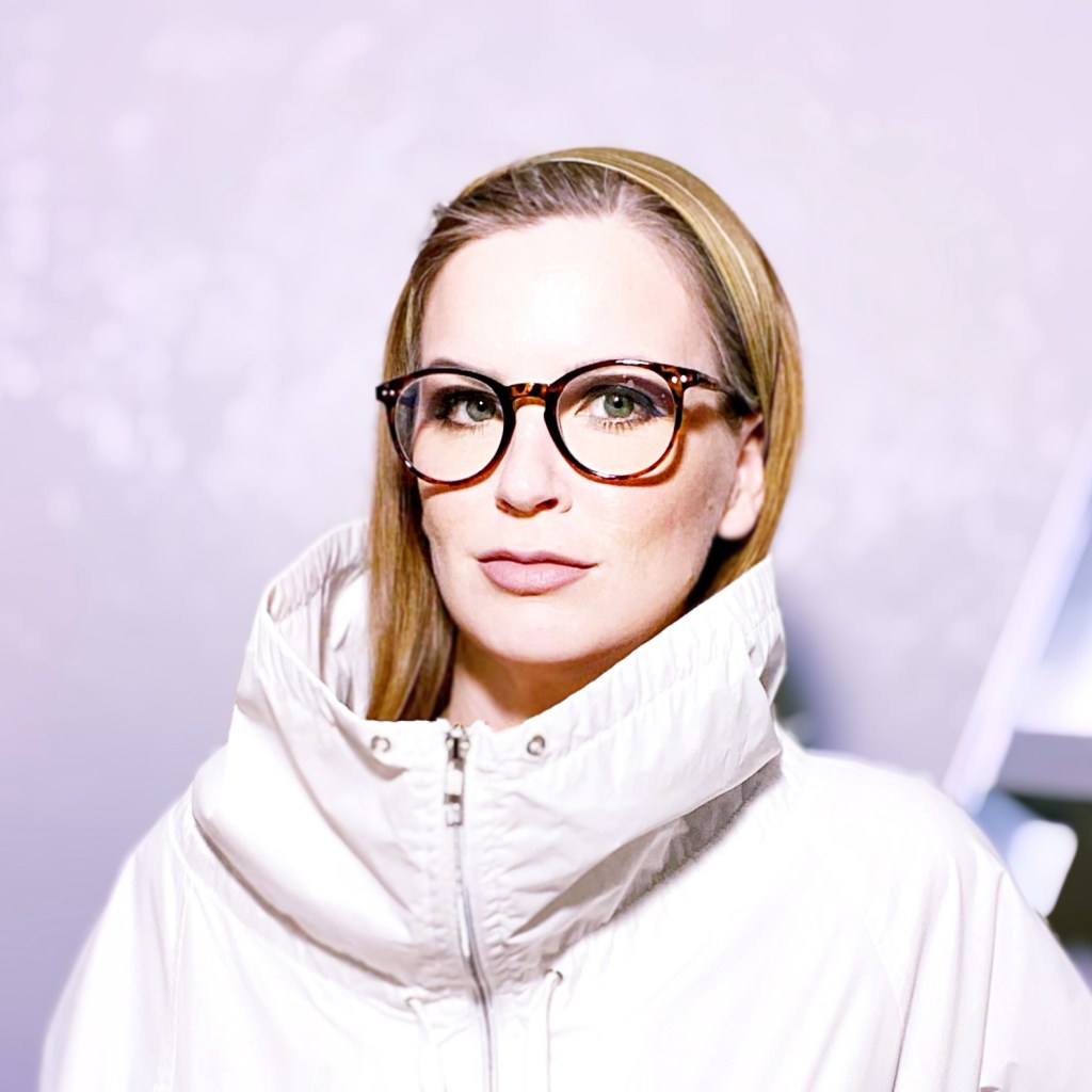 photo of Sade Reed wearing a white jacket standing in front of a purple wall